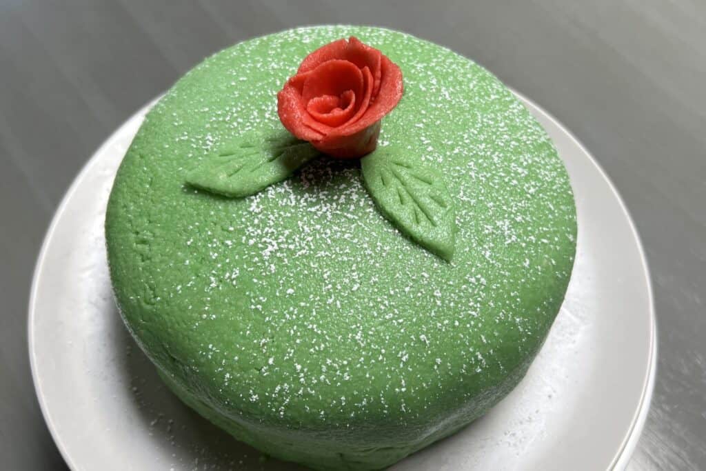 Whole green princess cake on white plate with red marzipan rose on top of cake