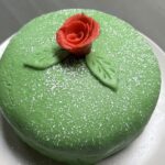 Whole green princess cake on white plate with red marzipan rose on top of cake