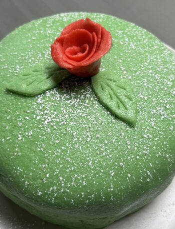 Whole green princess cake on white plate with red marzipan rose on top of cake