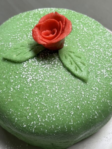 Whole green princess cake on white plate with red marzipan rose on top of cake