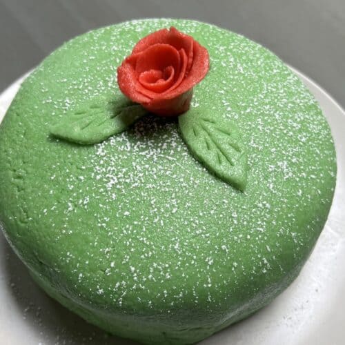 Whole green princess cake on white plate with red marzipan rose on top of cake