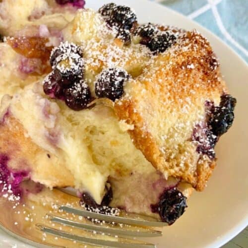 Blueberry cream cheese French toast on a white plate with a fork on the side