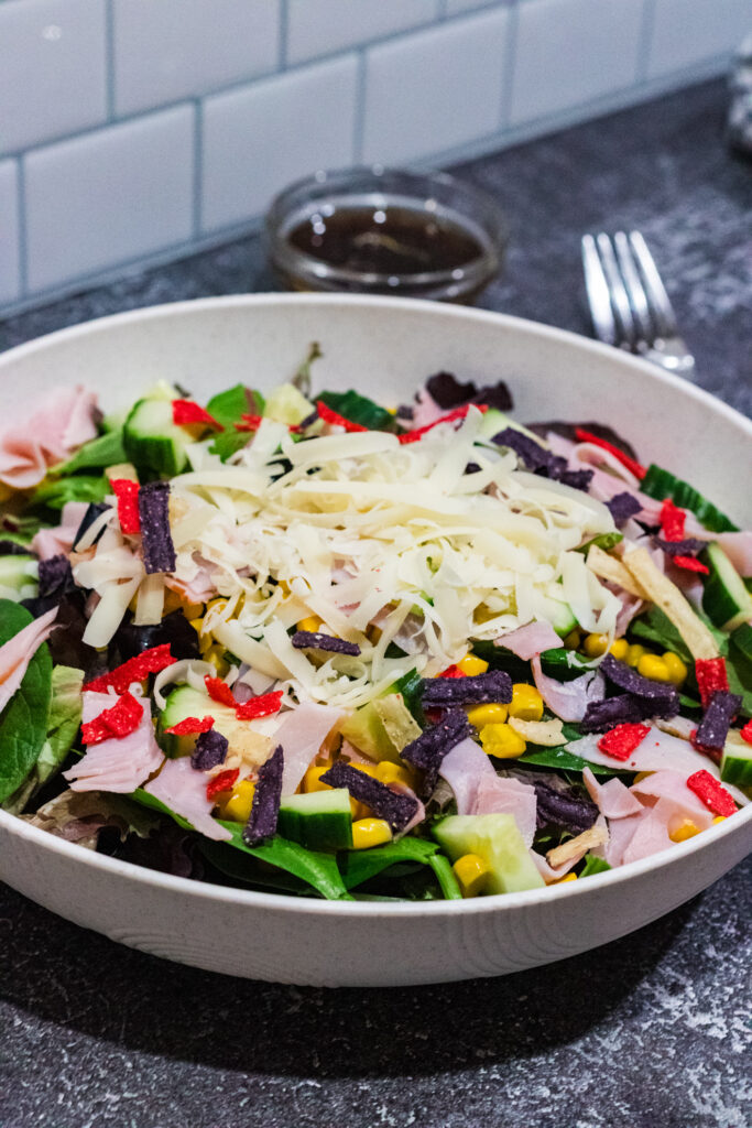 mixed freen salad with corn, tomatoes, shaved cheese, ham and tortilla strips