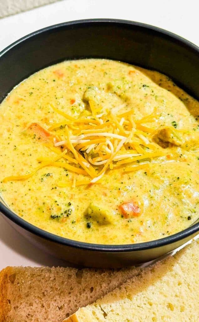 broocoli cheddar soup with some cheese sprinkled on top in a black bowl and 2 slices of bread in front