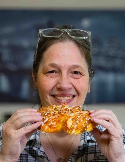 Debbie holding a bear claw pastry while smiling