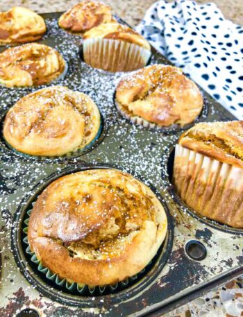 pumpkin cream cheese swirl muffins in a grey tin wrapped in paper forms on a table with a polkadot towel in the background