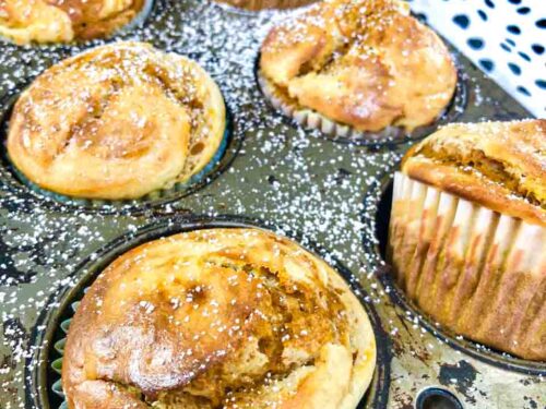 pumpkin cream cheese swirl muffins in a grey tin wrapped in paper forms on a table with a polkadot towel in the background