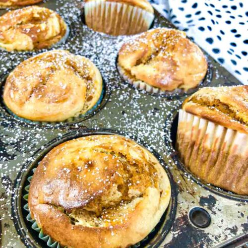 pumpkin cream cheese swirl muffins in a grey tin wrapped in paper forms on a table with a polkadot towel in the background