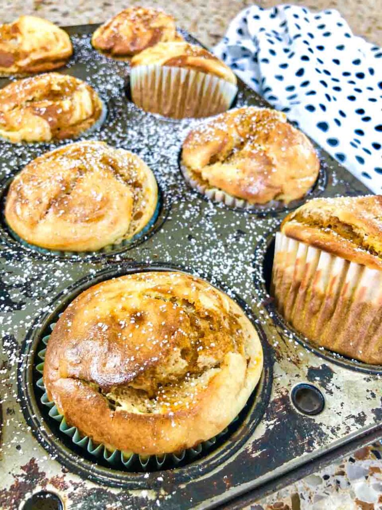 pumpkin cream cheese swirl muffins in a grey tin wrapped in paper forms on a table with a polkadot towel in the background