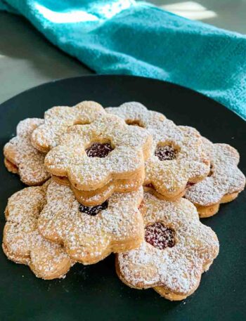 a black plate full of Linzer Tarts Cookies and a green towel in the background