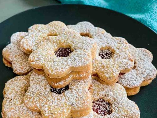 a black plate full of Linzer Tarts Cookies and a green towel in the background