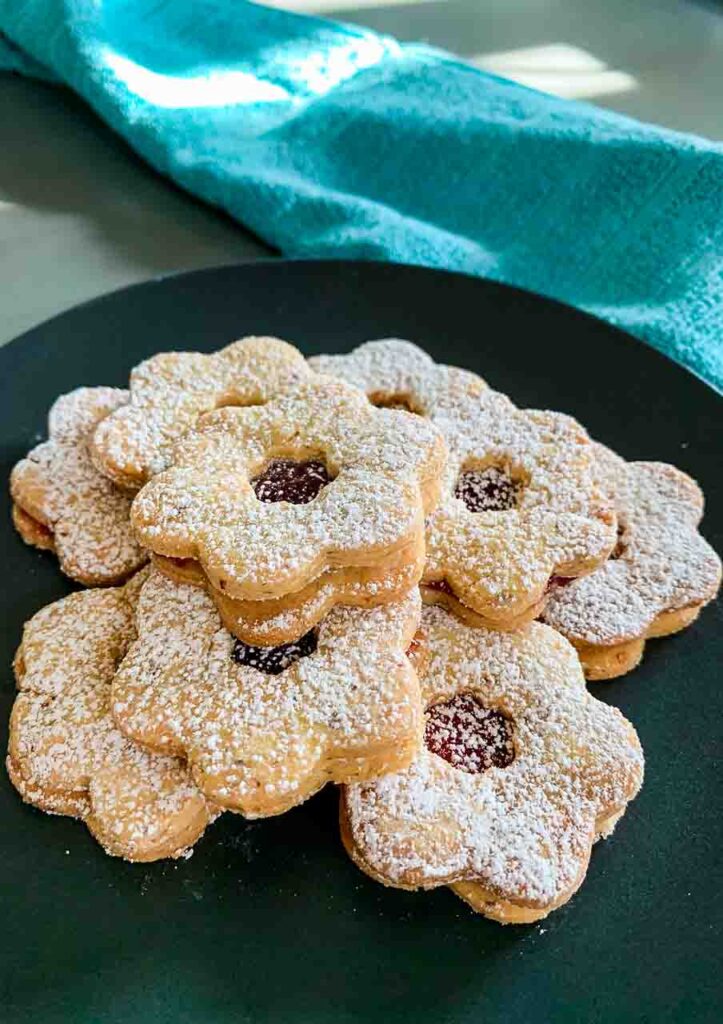 a black plate full of Linzer Tarts Cookies and a green towel in the background