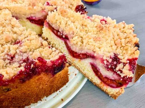 German plum cake as a whole on a cake platter with one piece sticking out on a cake shovel.