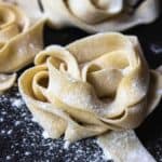 nest of home made uncooked pasta sprinkled with flour on a black board