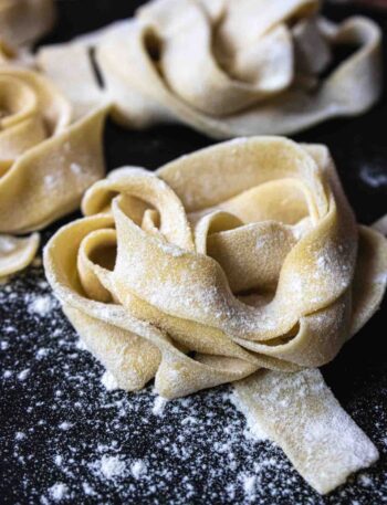 nest of home made uncooked pasta sprinkled with flour on a black board