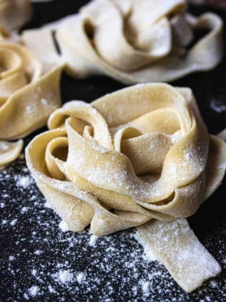 nest of home made uncooked pasta sprinkled with flour on a black board