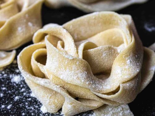 nest of home made uncooked pasta sprinkled with flour on a black board