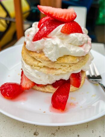 Strawberry Shortcake with cut up strawberries on top and in the middle together with fluffy whipped cream on a white plate