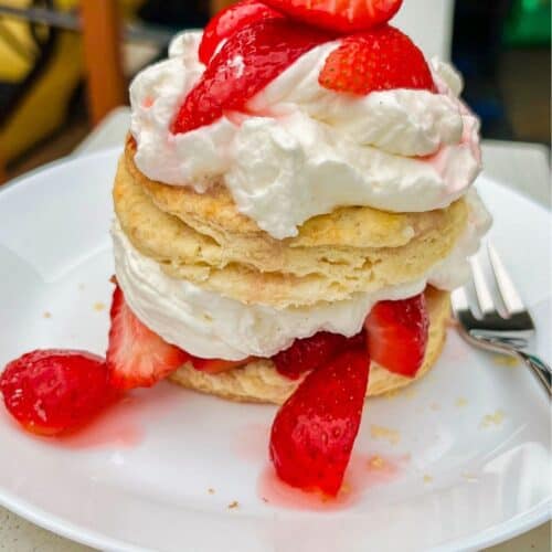 Strawberry Shortcake with cut up strawberries on top and in the middle together with fluffy whipped cream on a white plate