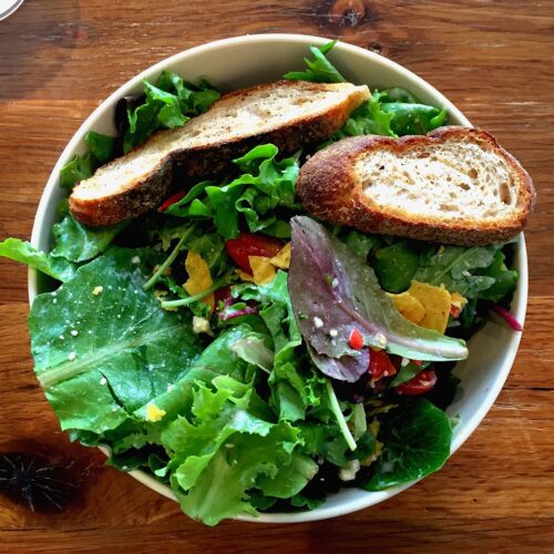 green mixed salad in a white bowl with small slices of bread