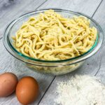 traditional German spätzle in a glass bowl and eggs with flour on the side