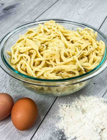 traditional German spätzle in a glass bowl and eggs with flour on the side