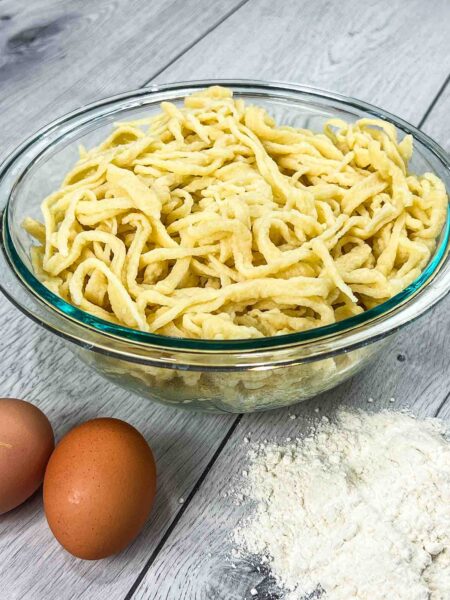 traditional German spätzle in a glass bowl and eggs with flour on the side