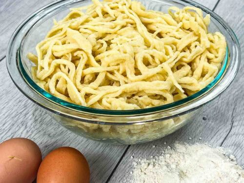 traditional German spätzle in a glass bowl and eggs with flour on the side