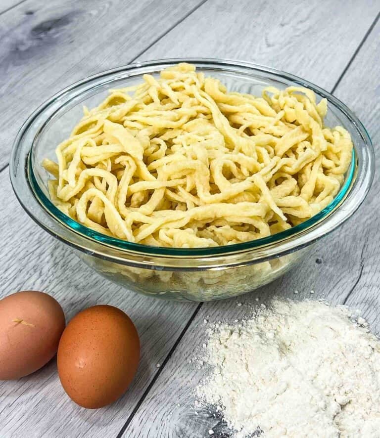 traditional German spätzle in a glass bowl and eggs with flour on the side