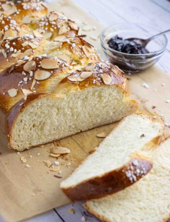 Hefezopf or German sweet bread laying on a parchment paper cut in slices with a glass of jam on the side