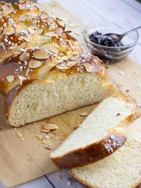 Hefezopf or German sweet bread laying on a parchment paper cut in slices with a glass of jam on the side