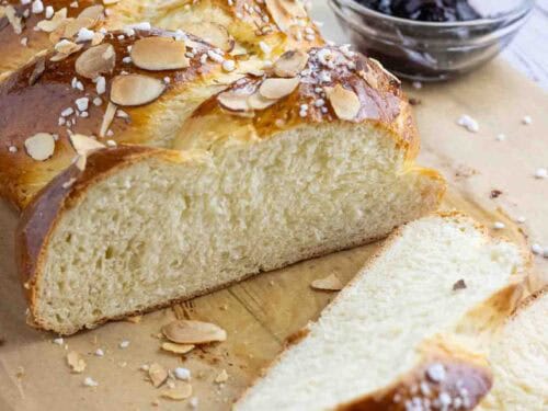 Hefezopf or German sweet bread laying on a parchment paper cut in slices with a glass of jam on the side