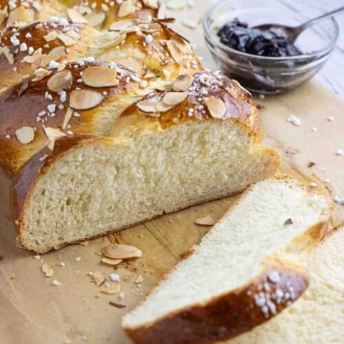 Hefezopf or German sweet bread laying on a parchment paper cut in slices with a glass of jam on the side