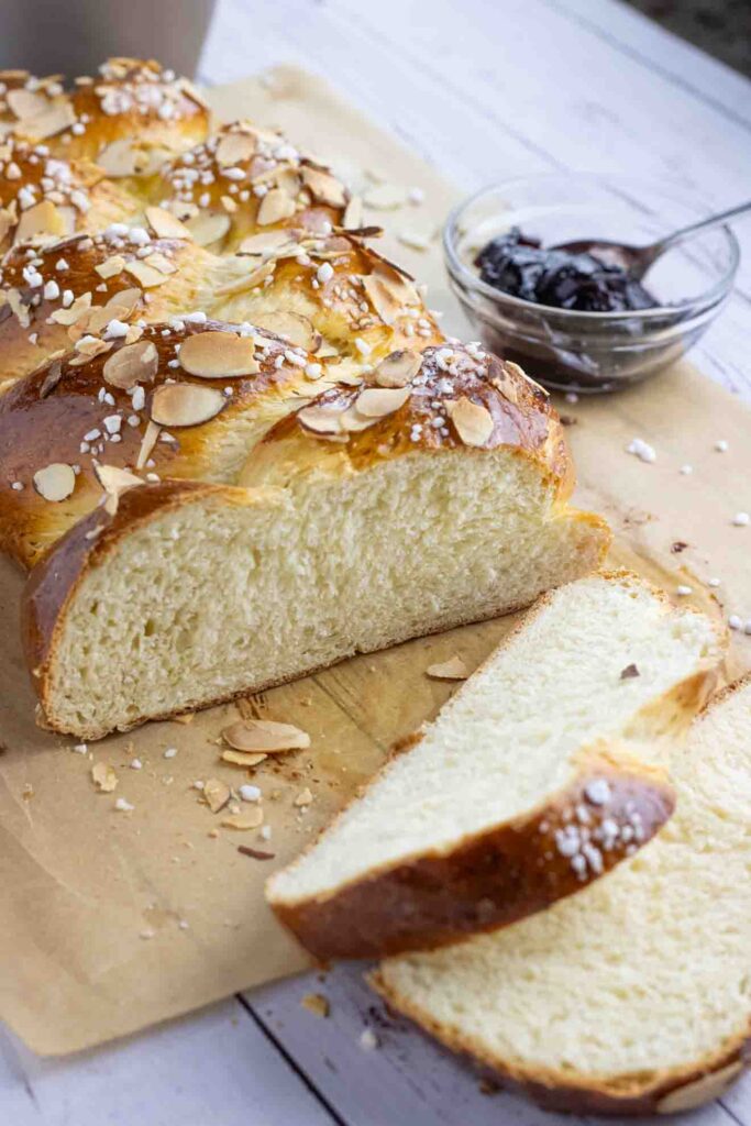 Hefezopf or German sweet bread laying on a parchment paper cut in slices with a glass of jam on the side