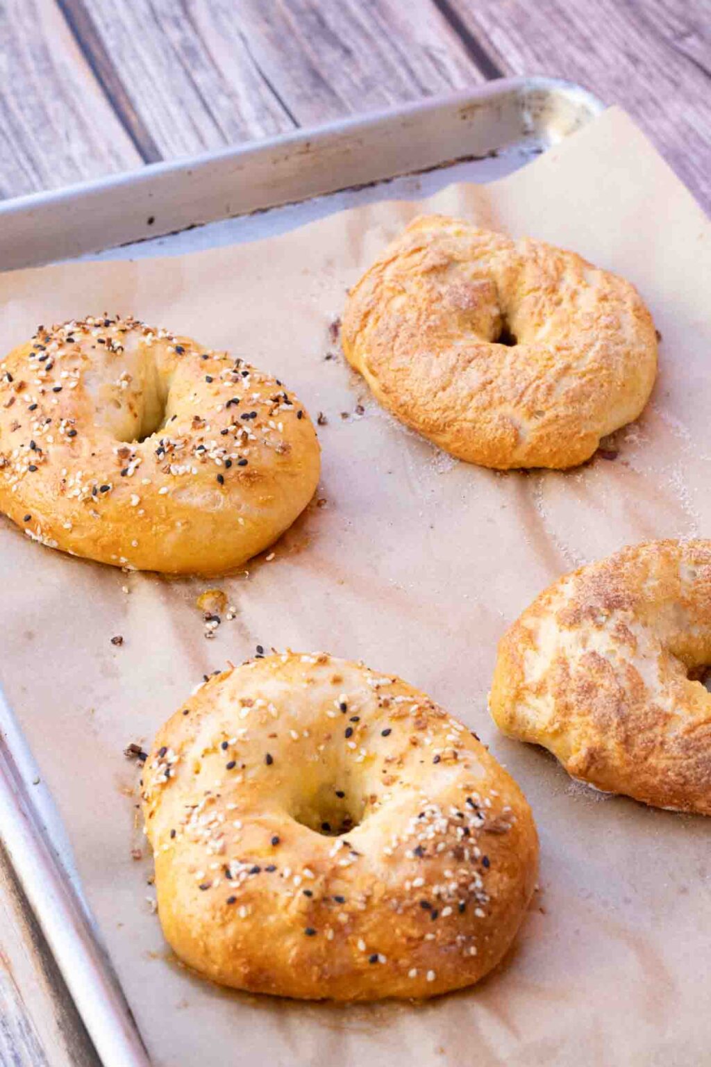 Bagels laying on a baking sheet with parchment paper underneath.