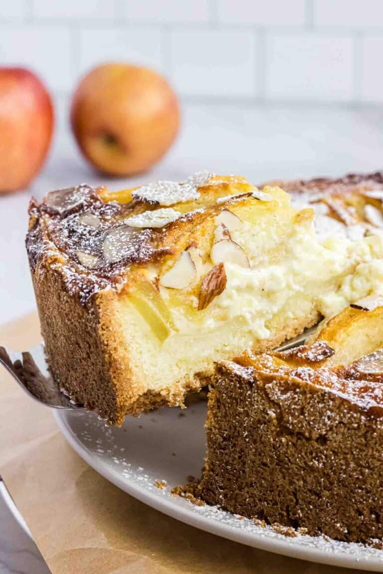 Apple cake on a plate with on slice elevated on a cake spoon. It shows its moist inside and has almond slices on the top.