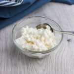 quark in a small glass bowl with a teaspoon on the side and a dark blue towel on the back of it.