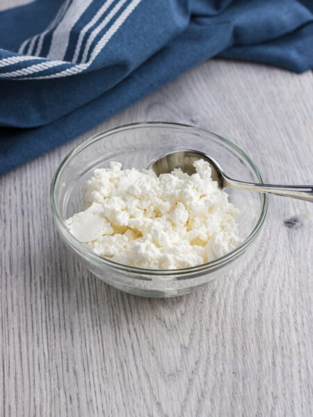 quark in a small glass bowl with a teaspoon on the side and a dark blue towel on the back of it.
