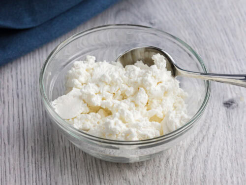 quark in a small glass bowl with a teaspoon on the side and a dark blue towel on the back of it.