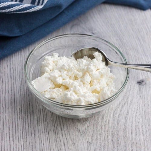 quark in a small glass bowl with a teaspoon on the side and a dark blue towel on the back of it.