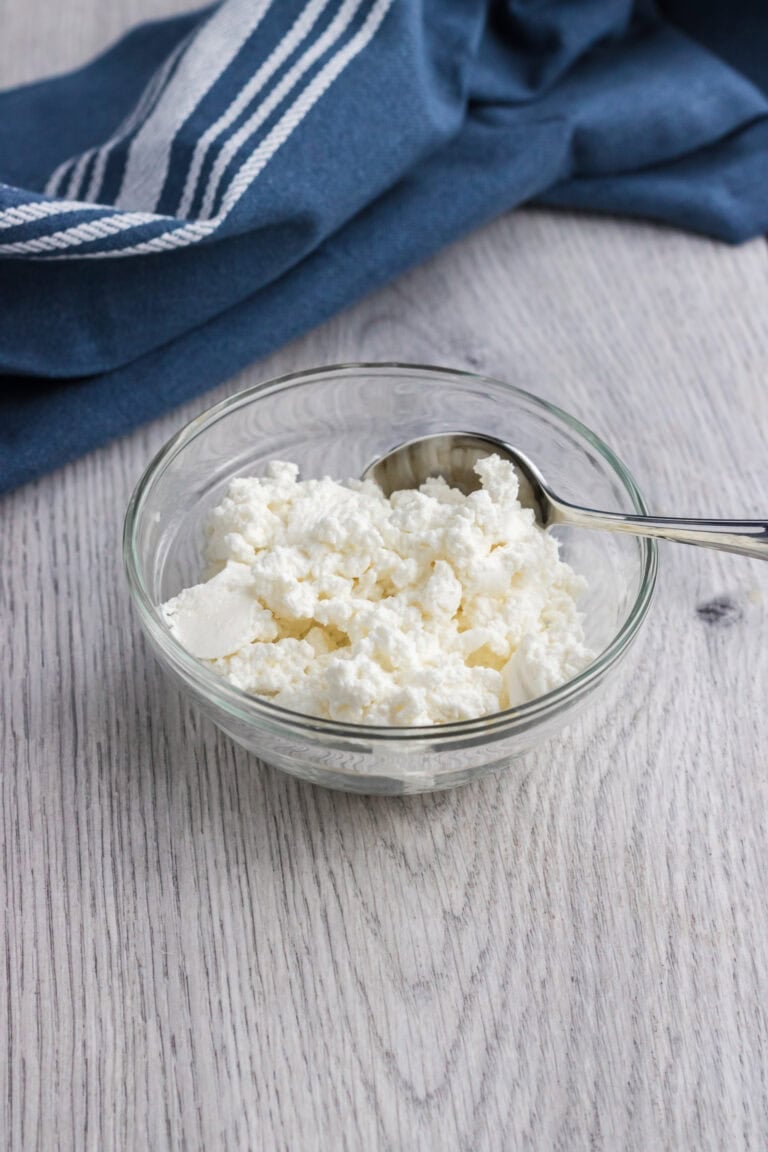 quark in a small glass bowl with a teaspoon on the side and a dark blue towel on the back of it.