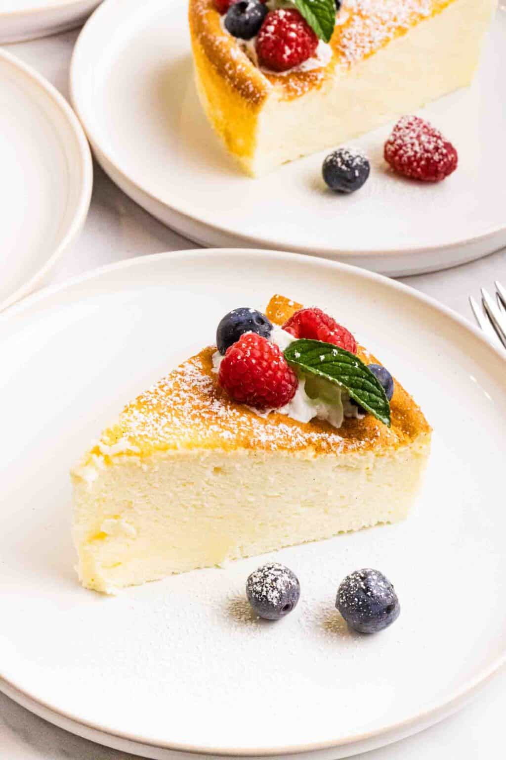 closeup of one piece of cake. Decorated with a swirl of whipping cream, 2 raspberries, 2 blueberries and a mint leave. 2 blueberries are on the front side on the white plate.