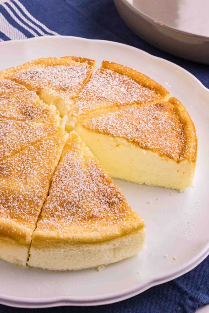 Fluffy Yogurt Cake on a white cake plate. Cake is topped with powdered sugar and one slice is missing.