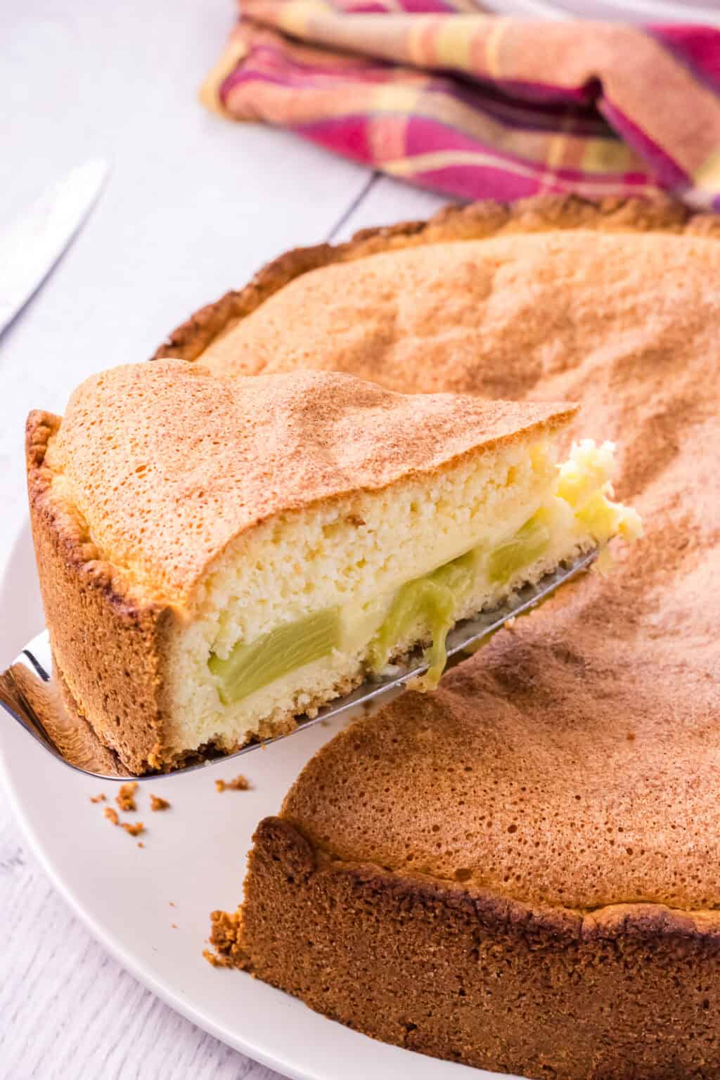 rhubarb cake slice is elevated over whole cake on cake shovel. Rhubarb pieces in cake can be clearly seen