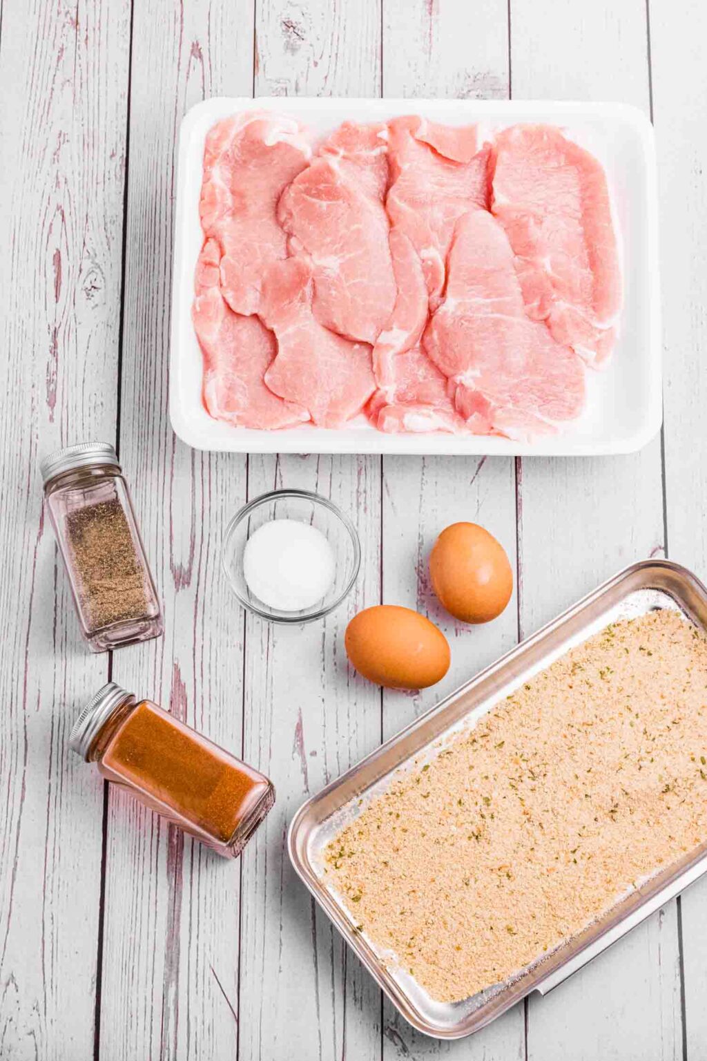 Wiener schnitzel Inrgedients on a white wood plank table. Pork Loin, 2 eggs, breadcrumbs, salt, pepper and paprika.