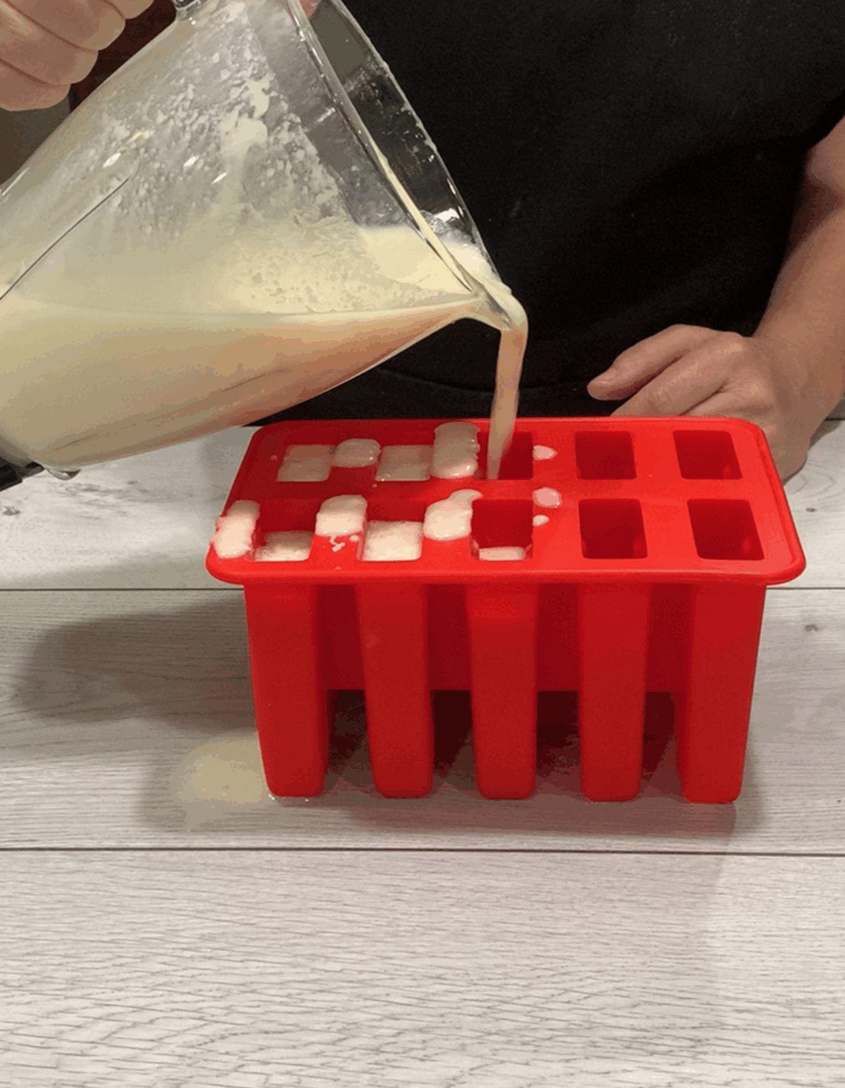 Filling in red popsicle molds with blended Pina colada blend.