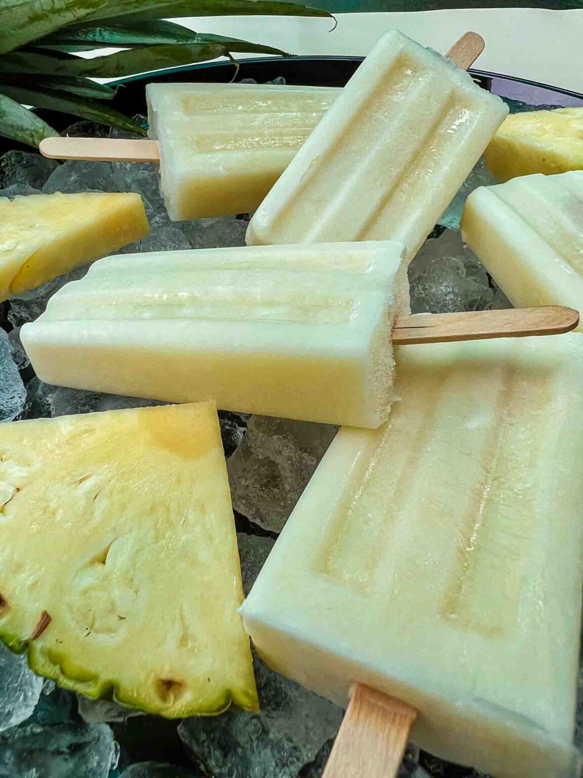 Extreme close-up of a creamy Pina Colada Popsicle with visible pineapple texture, resting on ice with fresh pineapple chunks nearby.
