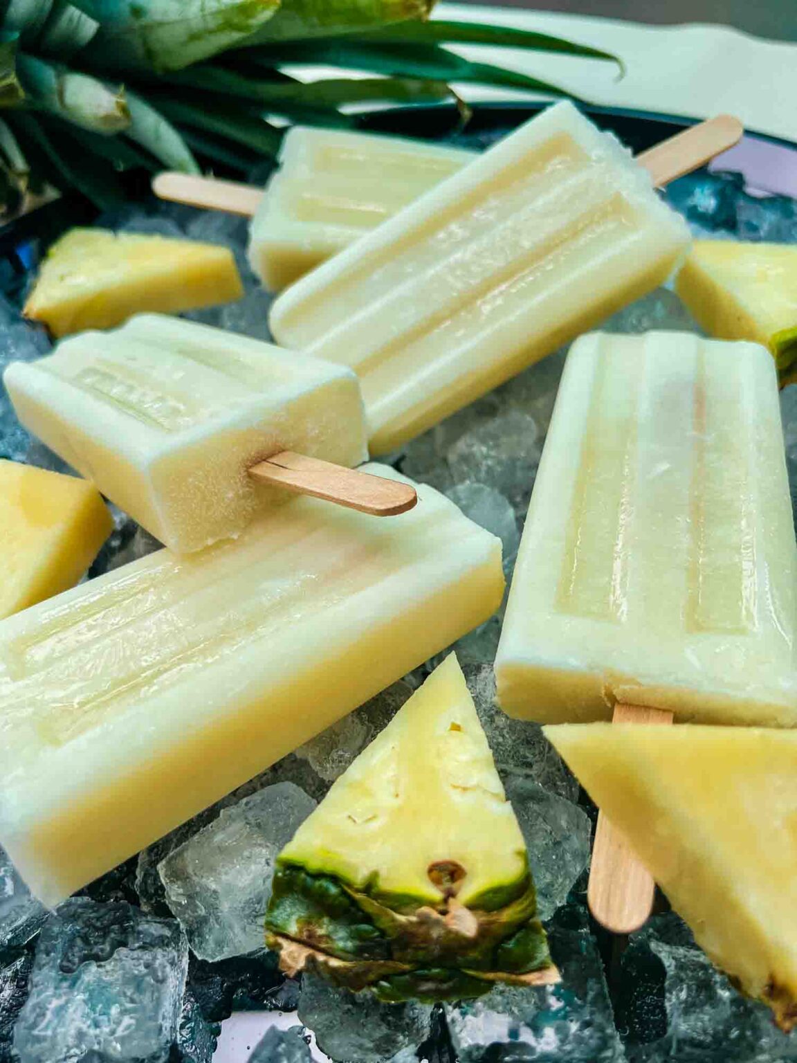 Close-up of creamy Pina Colada Popsicles resting on ice, with fresh pineapple chunks placed around for a tropical vibe.