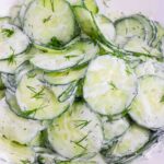 thin slices of English cucumbers in a white bowl coated with sour cream dill dressing
