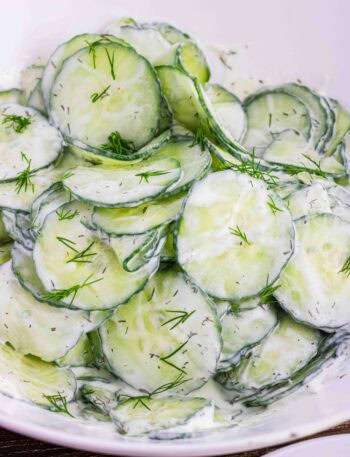 thin slices of English cucumbers in a white bowl coated with sour cream dill dressing